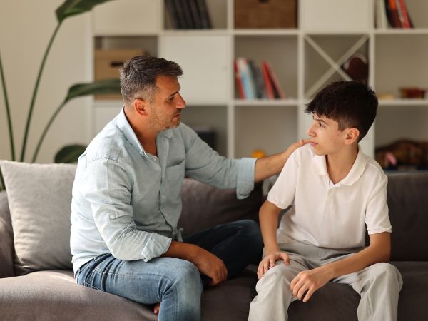 Padre che parla con il figlio per prepararlo emotivamente alla vacanza studio, rassicurandolo sulle difficoltà iniziali dei primi giorni Padre che parla con il figlio per prepararlo emotivamente alla vacanza studio, rassicurandolo sulle difficoltà iniziali dei primi giorni